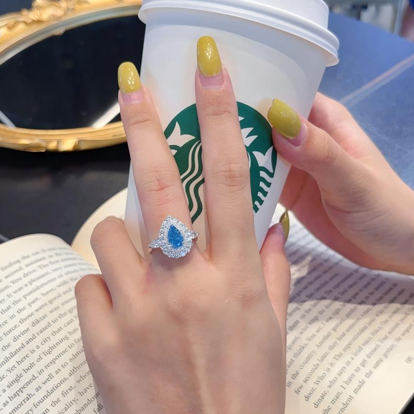 Pear blue halo ring worn on hand with white metal setting